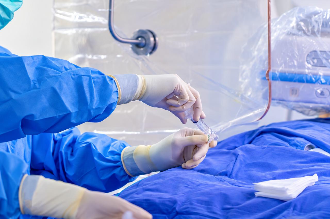 Equipe com luvas cirúrgicas manuseia dispositivo endovascular durante procedimento
